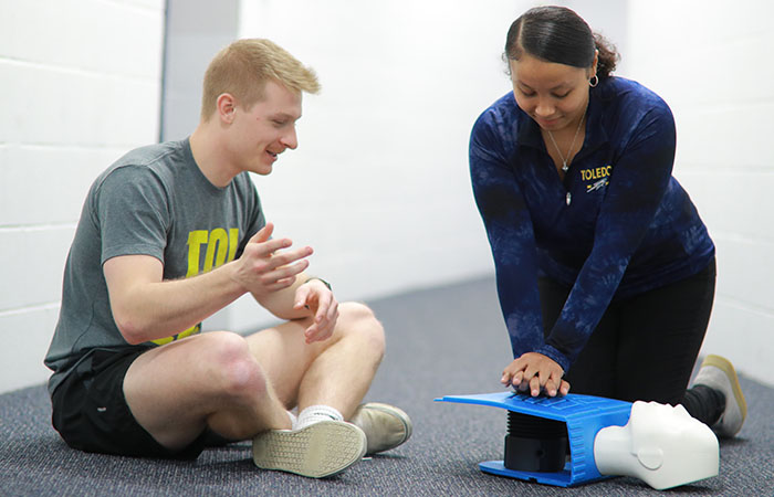 a young woman performing CPR on a dummy as a young man watches